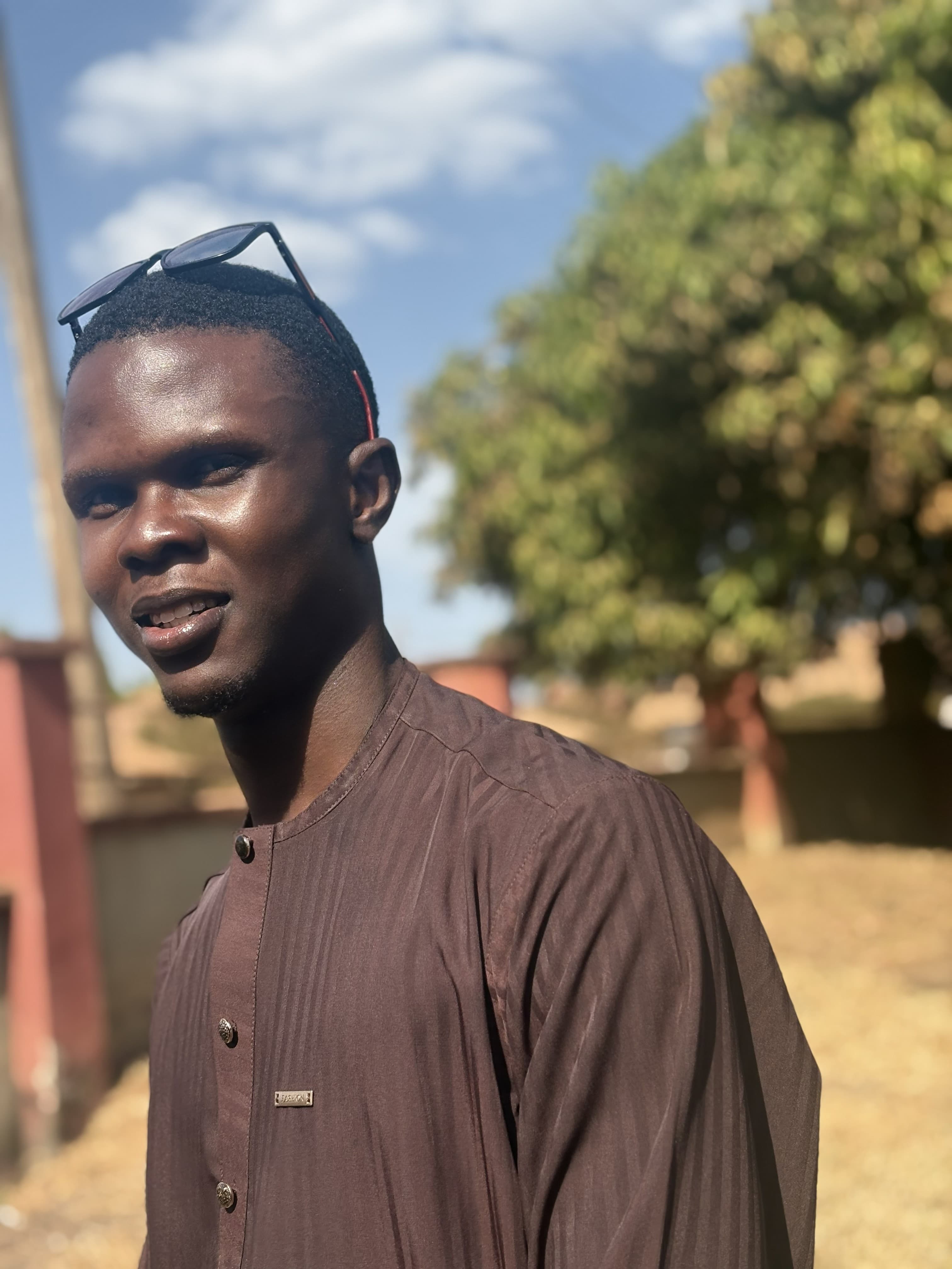 Portrait of Ayowande in a brown shirt, mango tree behind
